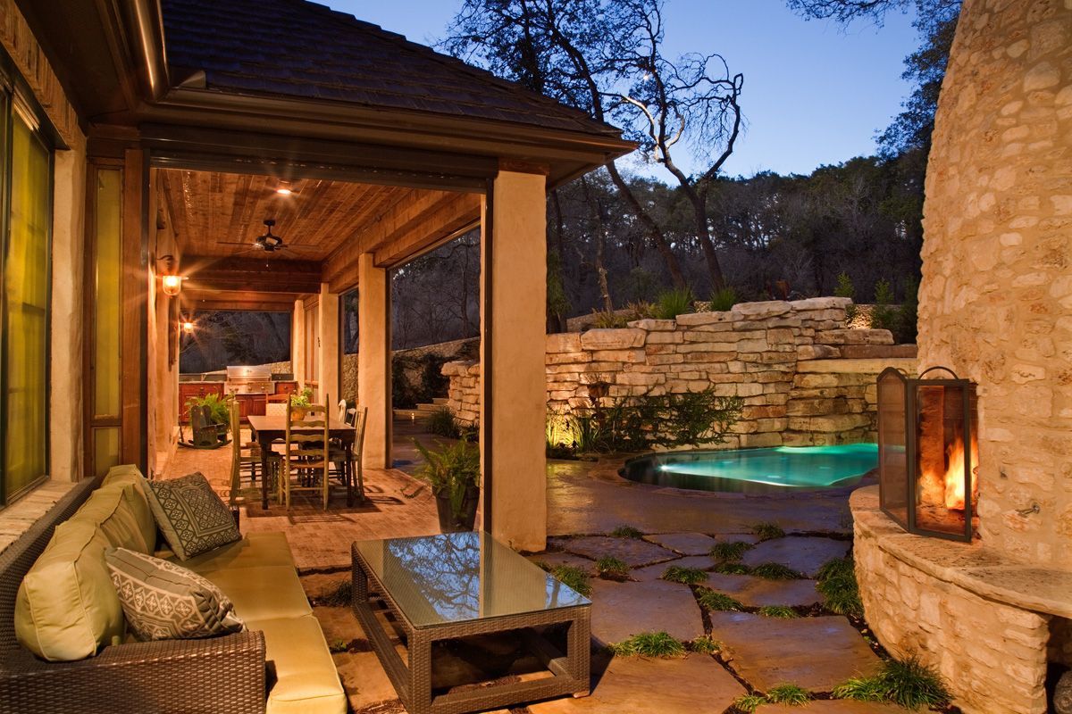 Outdoor patio with seating, table, fireplace, and pool at dusk.