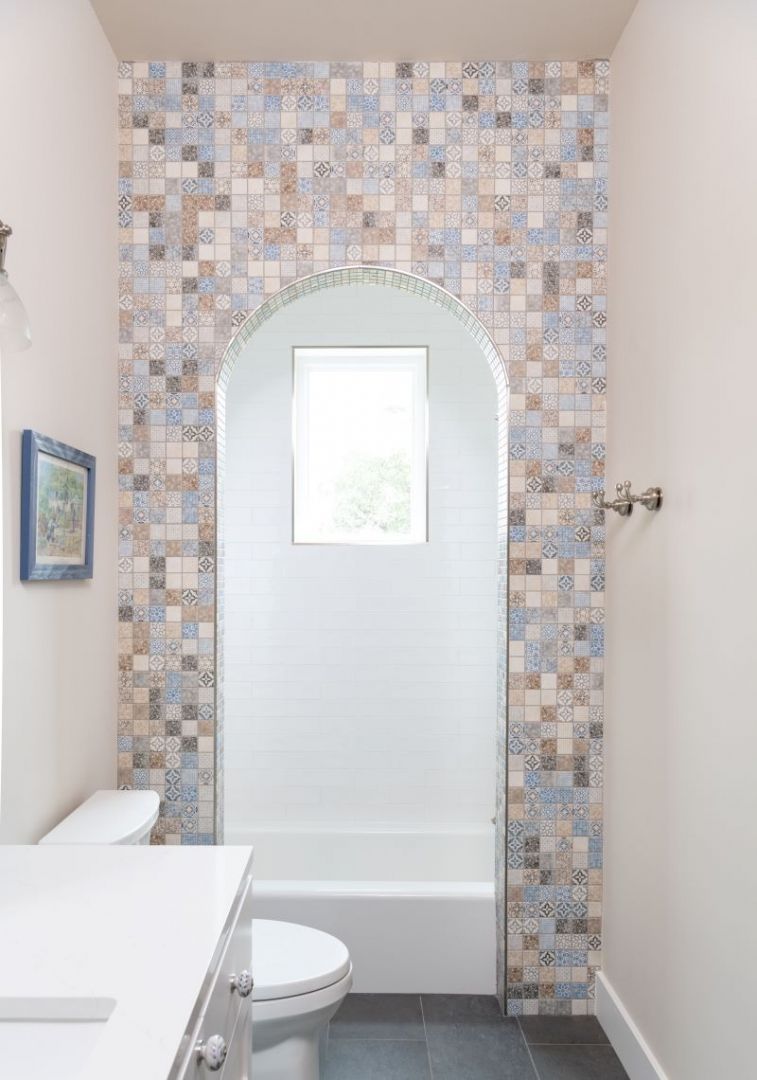 Bathroom with a tiled archway above a tub, neutral walls, and white fixtures.