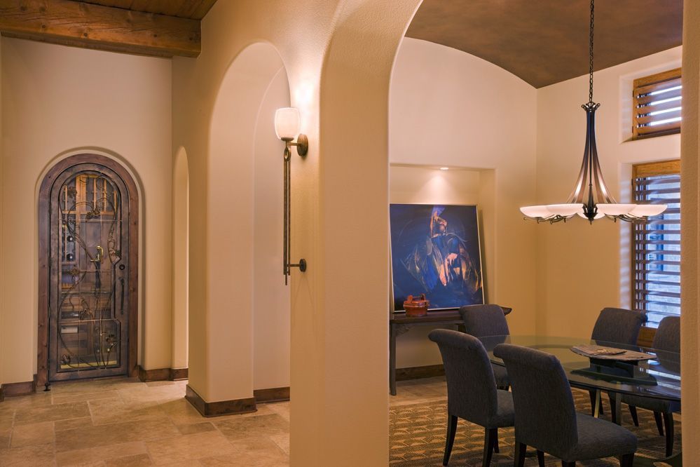 Interior of a home with archways, ornate wooden door, dining area with table, and light fixtures.