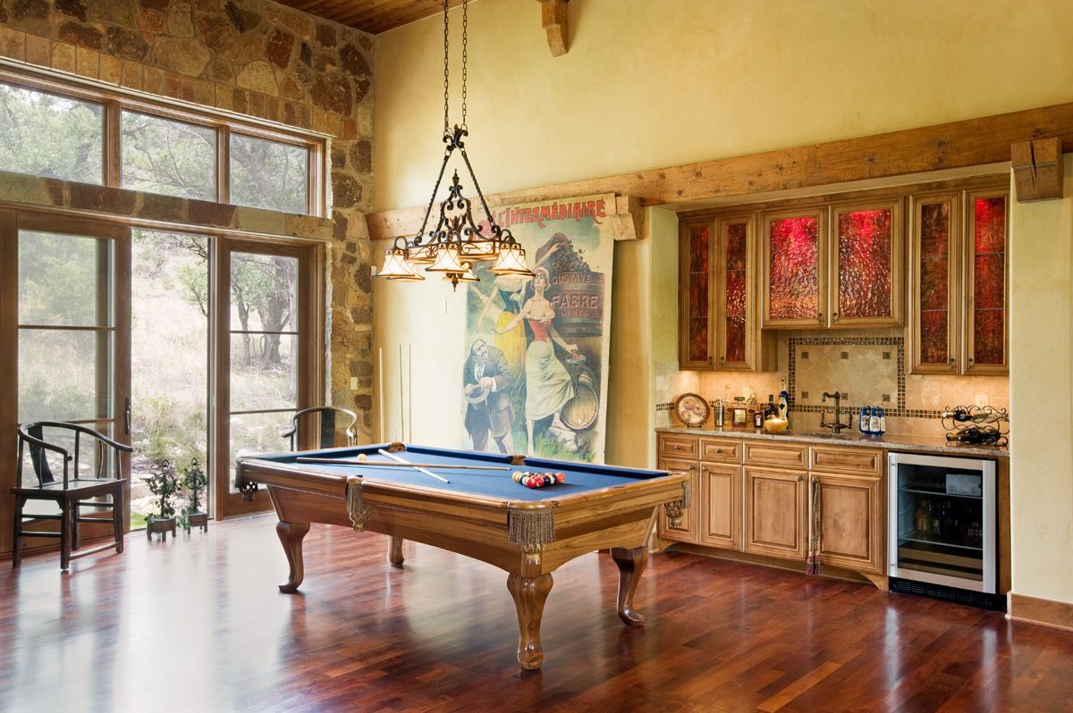 Pool table in room with bar, stone wall, and large window overlooking nature.