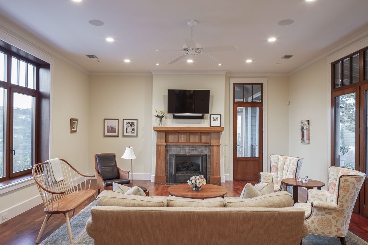 Living room with fireplace, furniture, and TV. Pale walls, wooden floors, and large windows.
