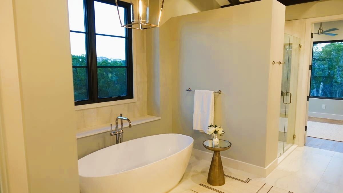 Bathroom with a white tub, window, gold accents, and a glass shower.