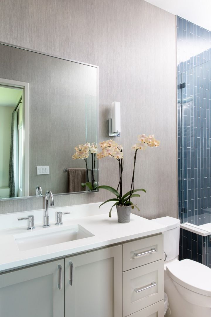 Modern bathroom with white vanity, orchid, large mirror, and dark blue tiled shower.