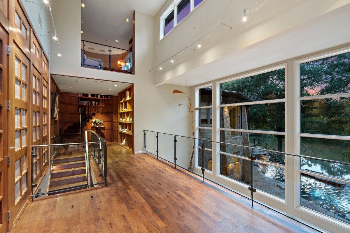 Spacious home interior: hardwood floor, large windows, glass railing, wooden doors, stairs, and high ceilings.