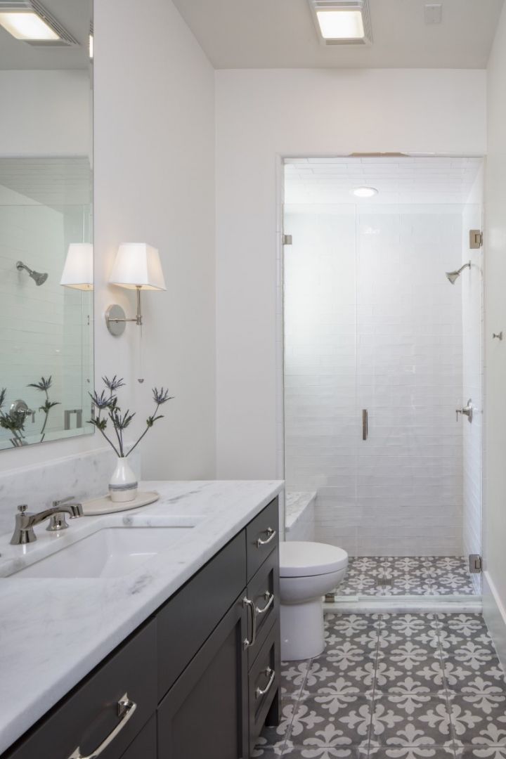 Modern bathroom with a vanity, walk-in shower, toilet, and patterned floor. White walls and dark gray cabinets.