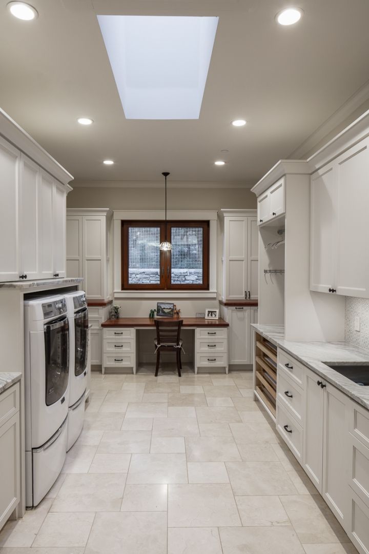 Bright laundry room with white cabinets, stacked washer/dryer, desk, and skylight.