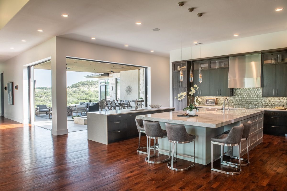 Modern kitchen with island and bar stools opening to an outdoor dining area.