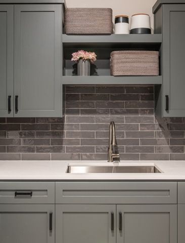 Gray cabinets with floating shelves above a stainless steel sink and brick backsplash.
