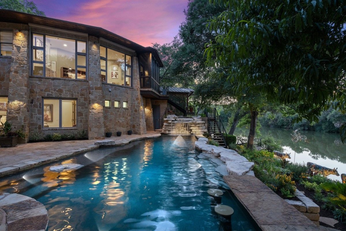 Luxury home with a pool overlooking a river at sunset.