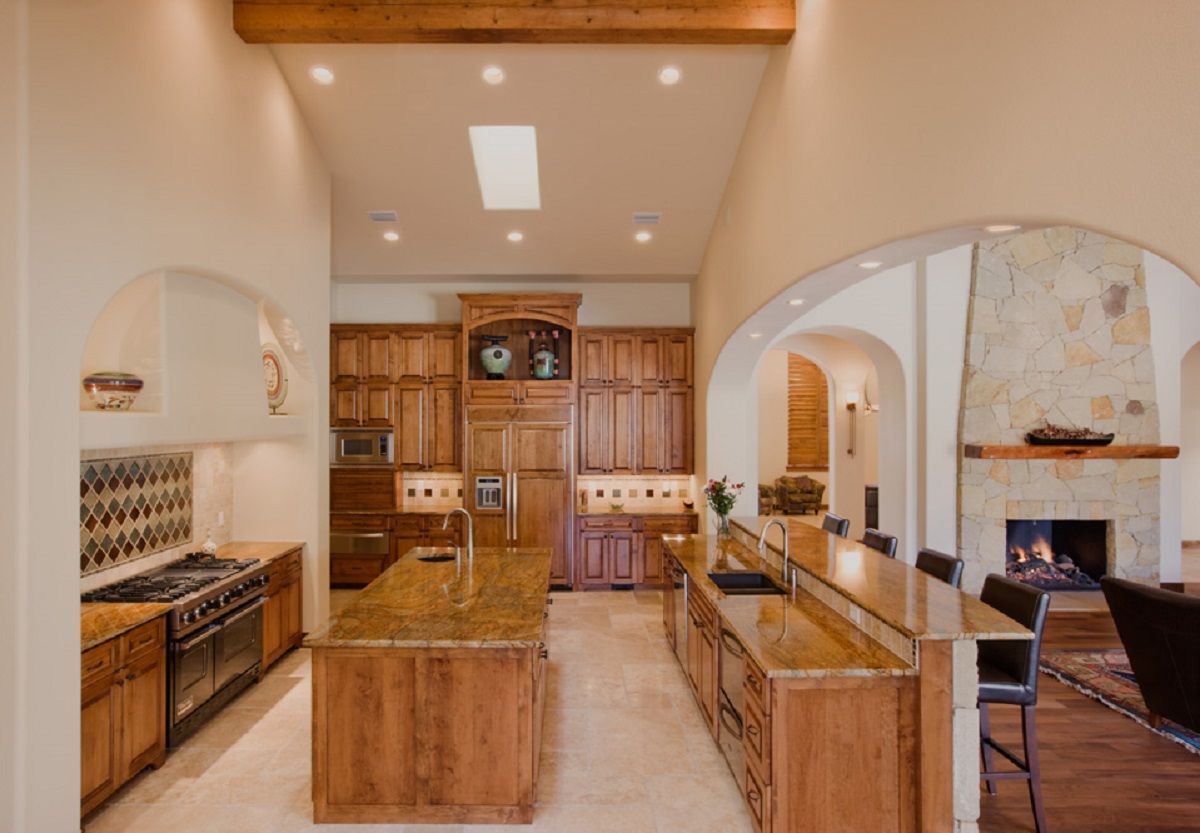 Spacious kitchen with wood cabinetry, granite counters, and an open archway to a fireplace.