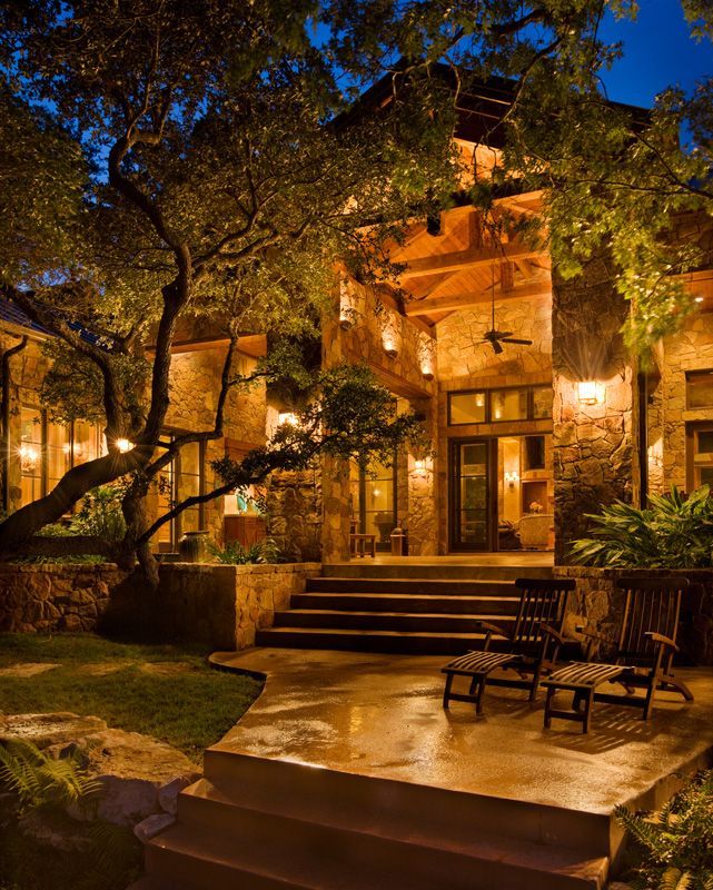 Stone house exterior at night with illuminated trees and patio furniture.