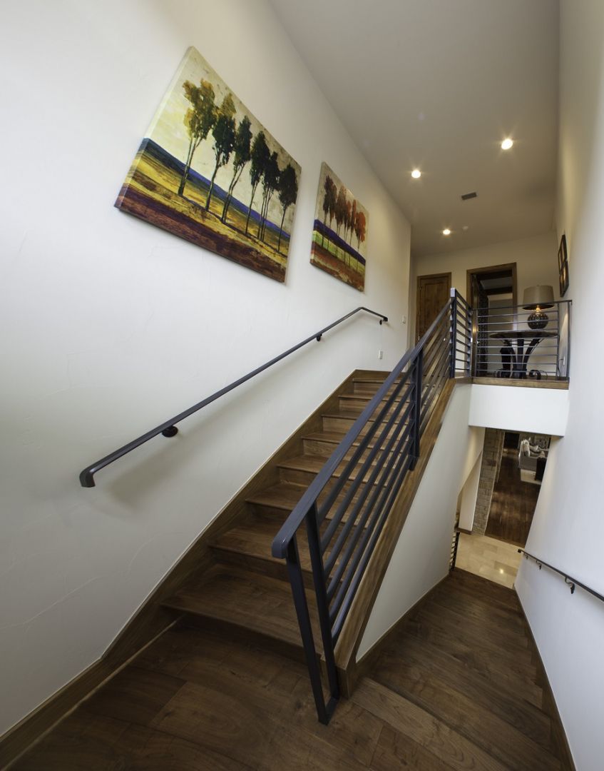 Wooden staircase with metal railing; artwork on white wall.