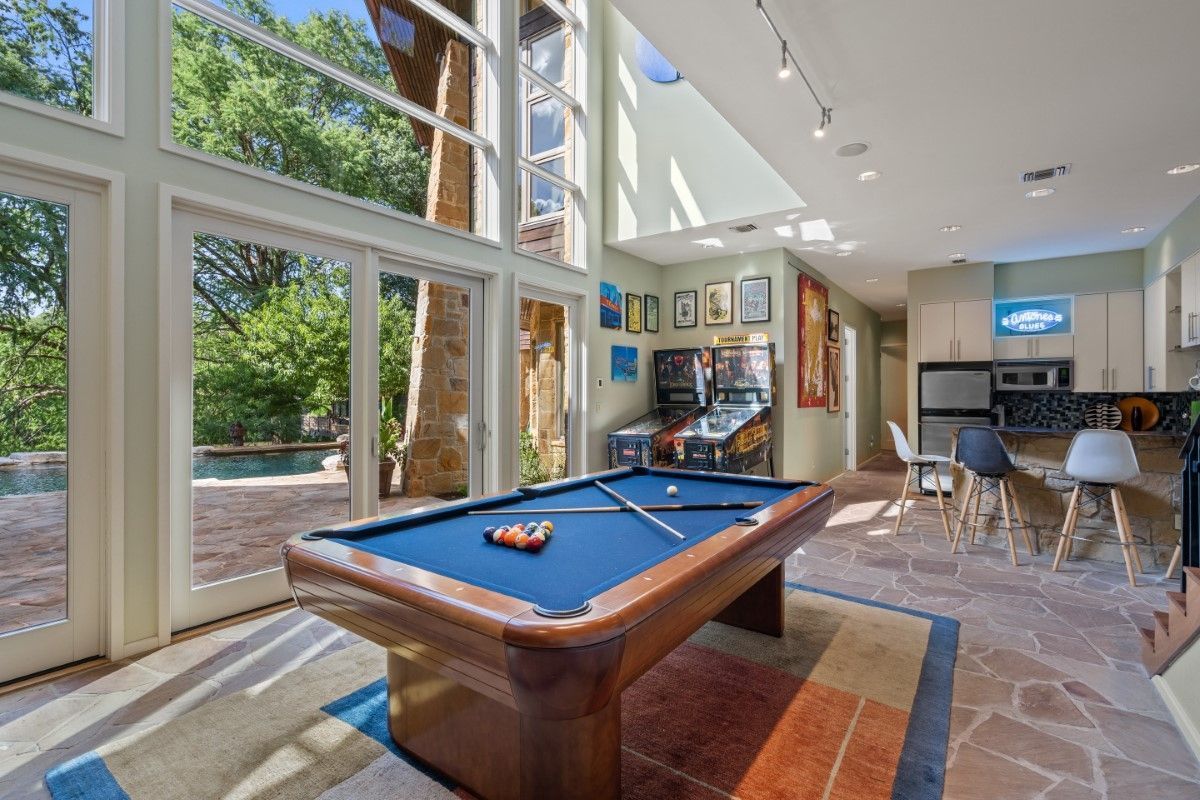 Pool table in a modern room with large windows overlooking a patio and trees.
