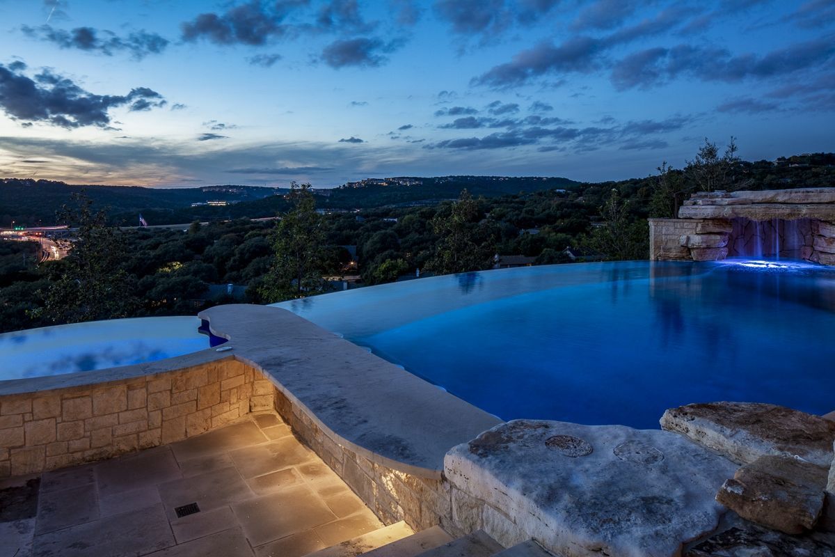 Infinity pool overlooking a dark landscape, with blue water reflecting the twilight sky.
