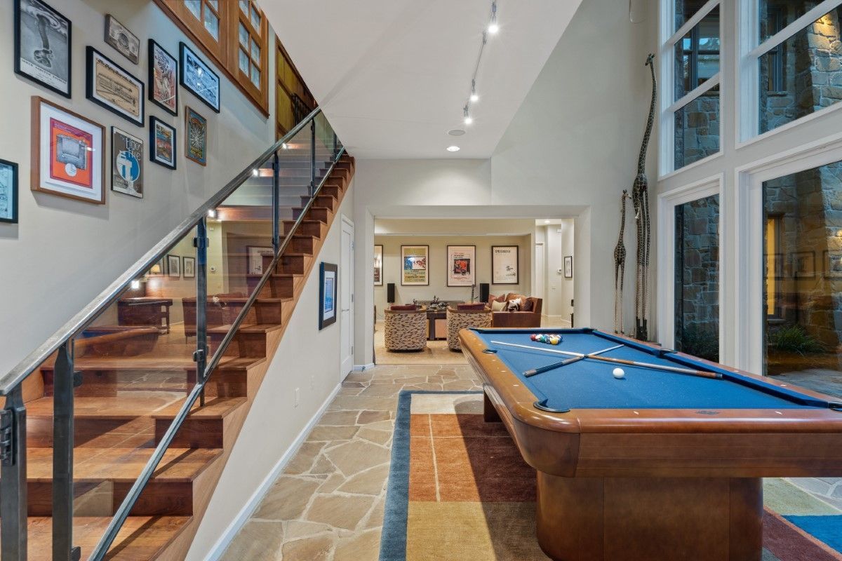 Game room with pool table, staircase, and artwork on the wall, natural stone flooring, and large windows.