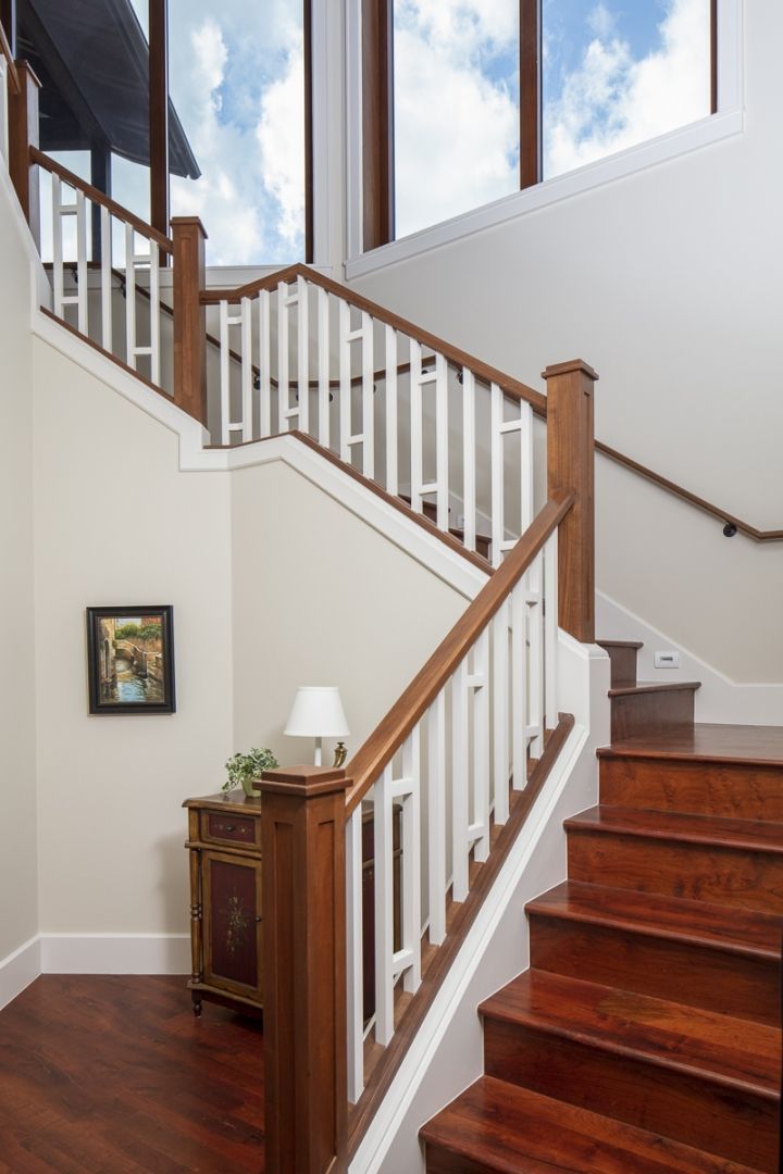 Staircase with wooden steps and white banisters, leading to a tall window with blue sky.