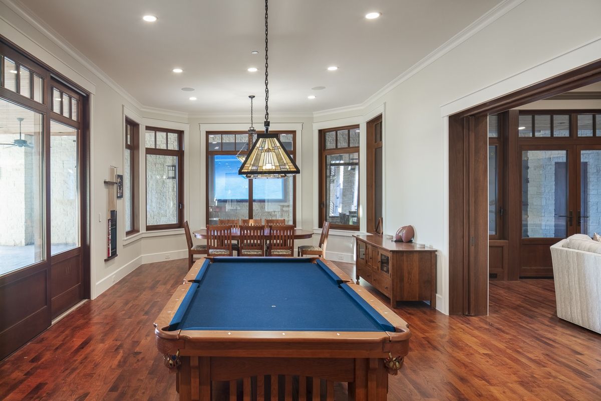 Pool table in a sunlit game room with dark wood trim, bay windows, and a view of the outdoors.