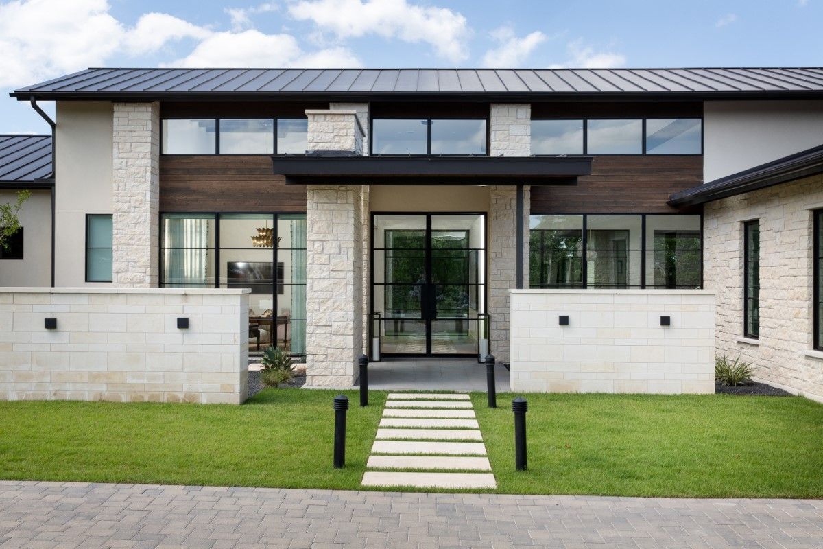 Modern home exterior with stone facade, dark roof, and black-framed glass doors and windows.