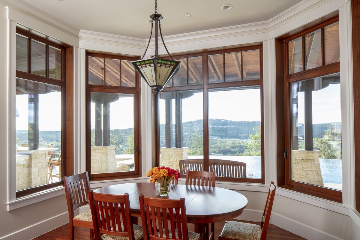Dining room with wood-framed windows, round table, and chairs. View of outdoors.