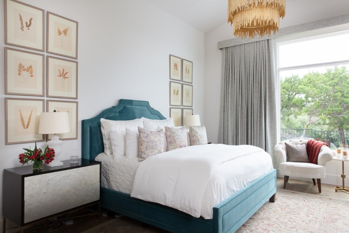 Teal bed, white bedding, art above. White walls, large window with drapes, gold chandelier.