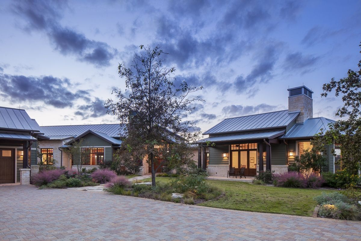 Stone home with a driveway and landscaped yard, under a cloudy sky at dusk.