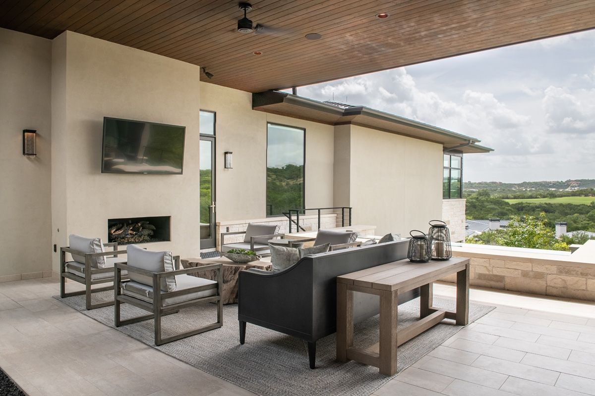 Covered outdoor living space with modern furniture, fireplace, and scenic view.