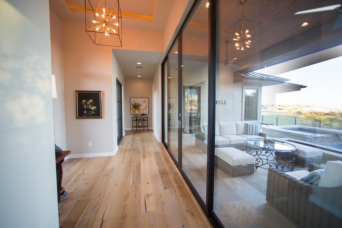 Hallway with wood floors, glass wall to outdoor patio with seating, art on wall.