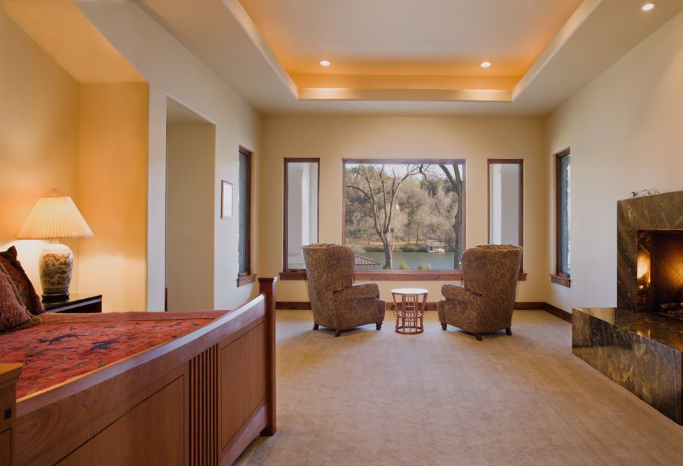 Spacious bedroom with bed, chairs facing window, fireplace, and neutral-toned walls and carpet.