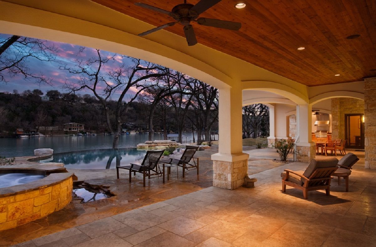 Patio with pool, lake view at dusk. Chairs on stone patio, under arched roof.