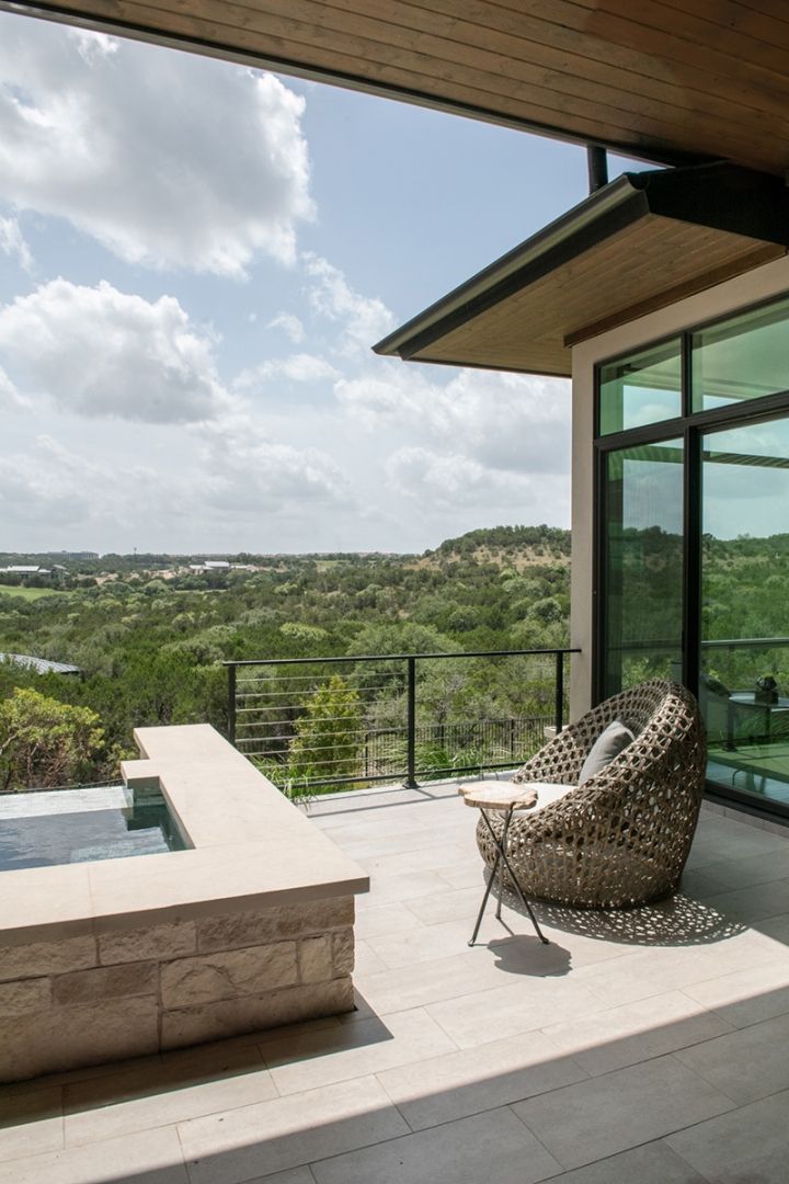 Patio with a woven chair, small table, and view of green hills and blue sky.