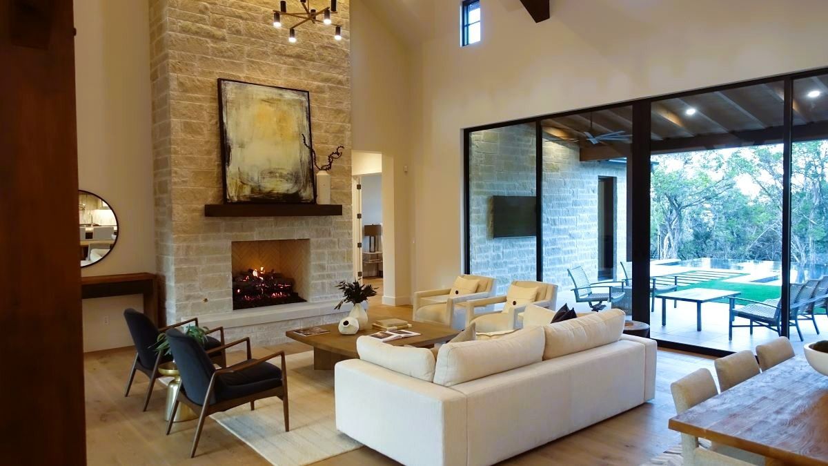 Living room with stone fireplace, white sofa, large windows overlooking a patio.