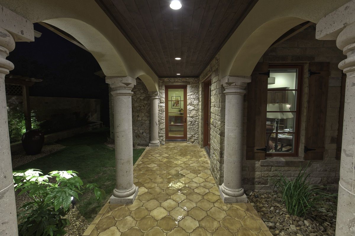 Covered walkway with stone columns and arches, leading to a door at night.
