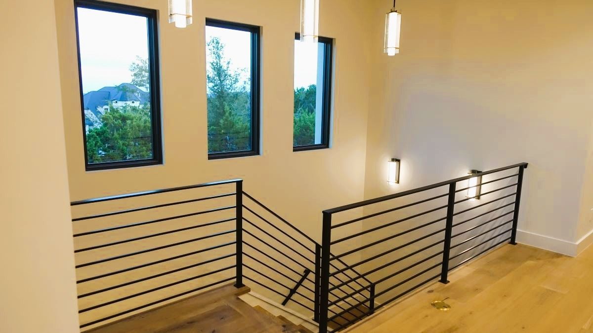Staircase with horizontal black railings, three windows, and pendant lights.