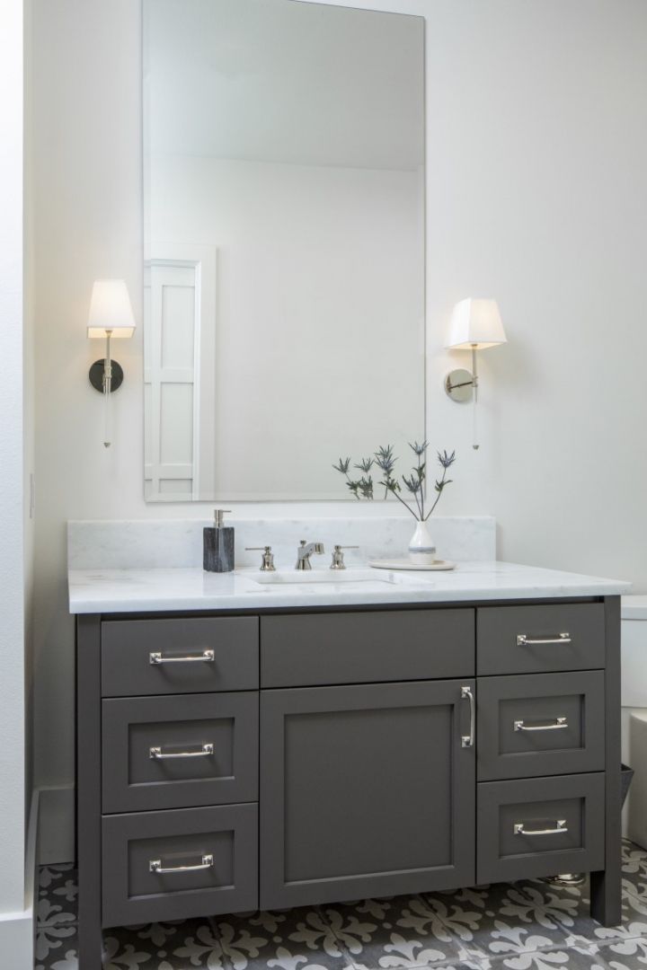 Bathroom with gray vanity, large mirror, and sconce lights. Marble countertop and patterned floor.