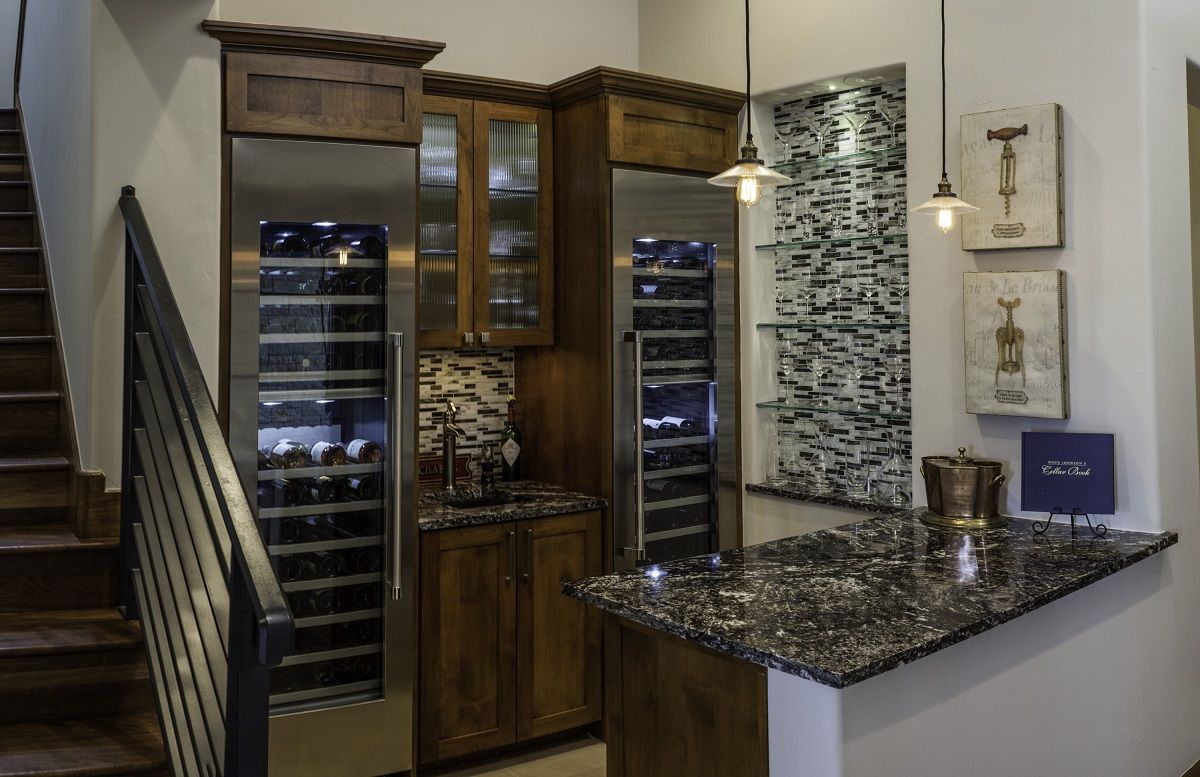 A wine bar with wood cabinets, a granite countertop, and a built-in wine cooler next to stairs.