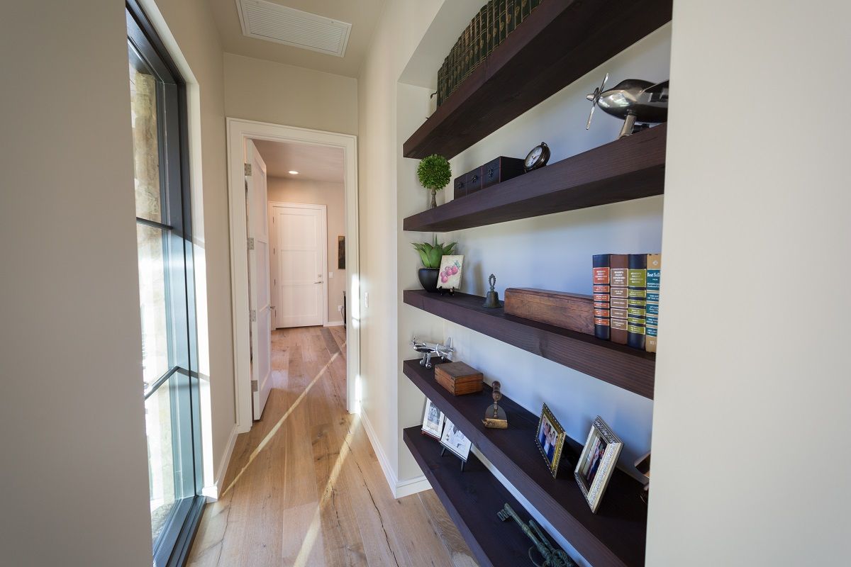 Hallway with built-in shelves displaying decor; light wood floors, white walls, natural light.