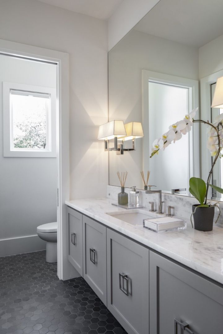 Gray bathroom with gray vanity, marble countertop, and large mirror, with an orchid and light fixture.