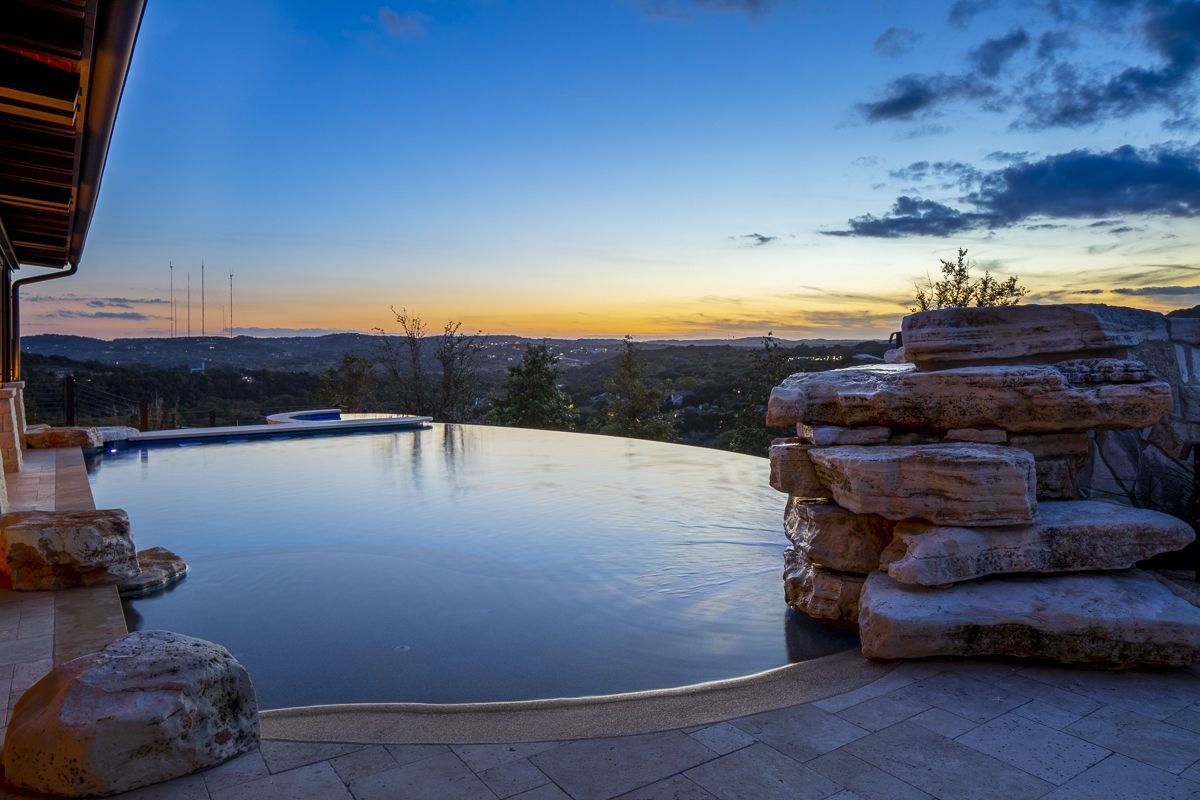 Infinity pool overlooking a landscape at sunset. Rocks surround the pool's edge.