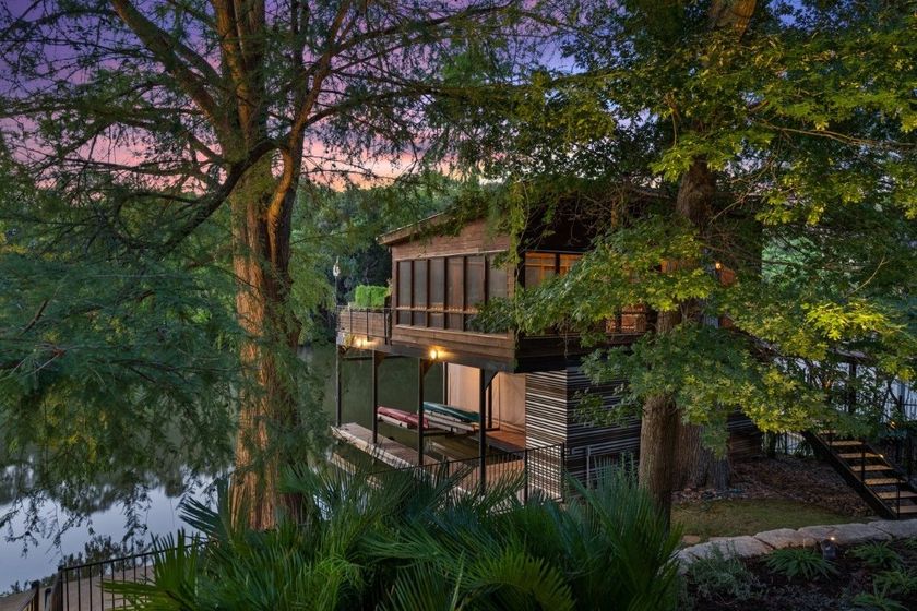 Boathouse on a lake at dusk, surrounded by trees. Stone and wood structure with a deck.