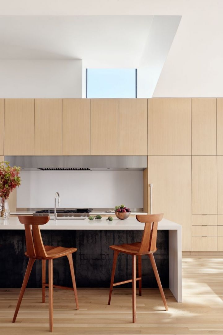 Modern kitchen with light wood cabinets, island, and two wooden bar stools.