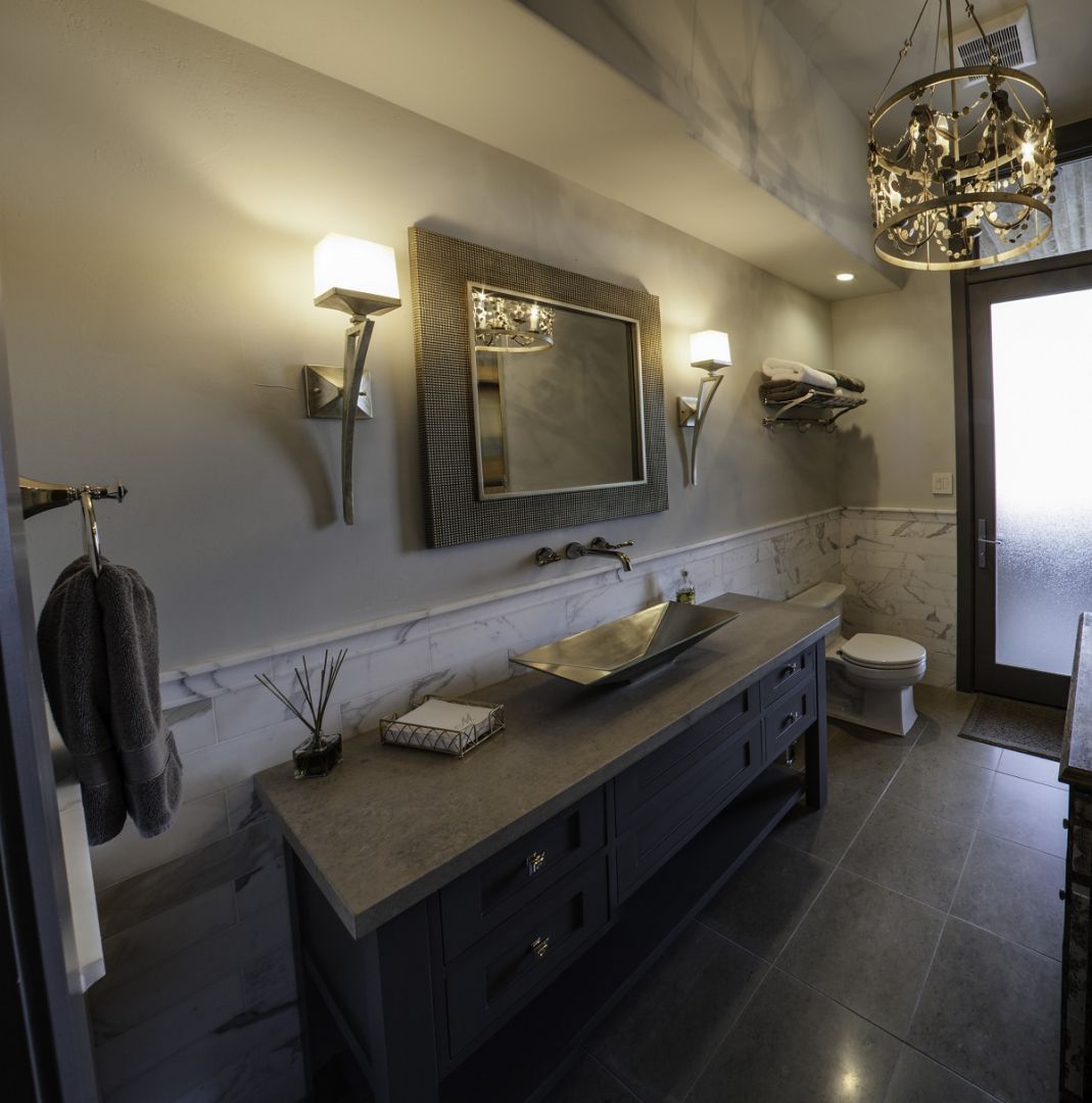 Bathroom with gray cabinets, large mirror, sconces, and ornate chandelier.