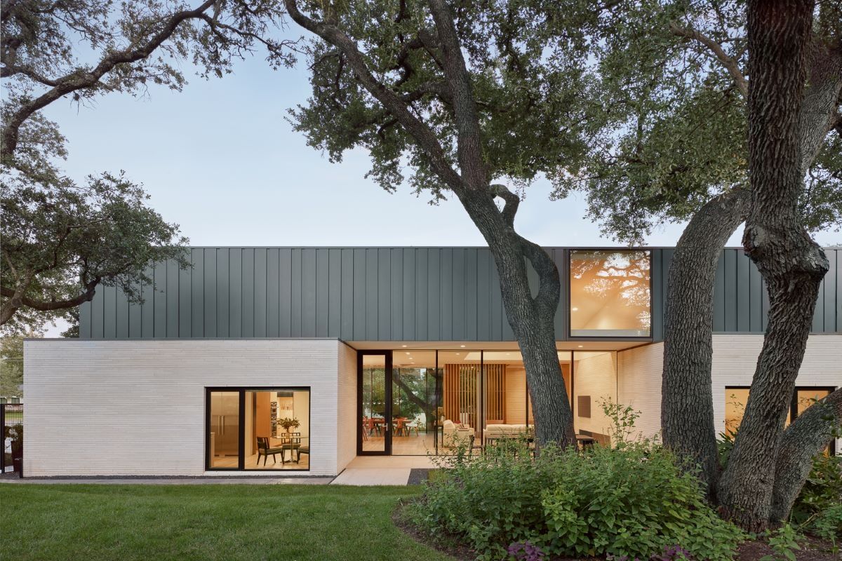 Modern home exterior with neutral facade, large windows, and mature trees.