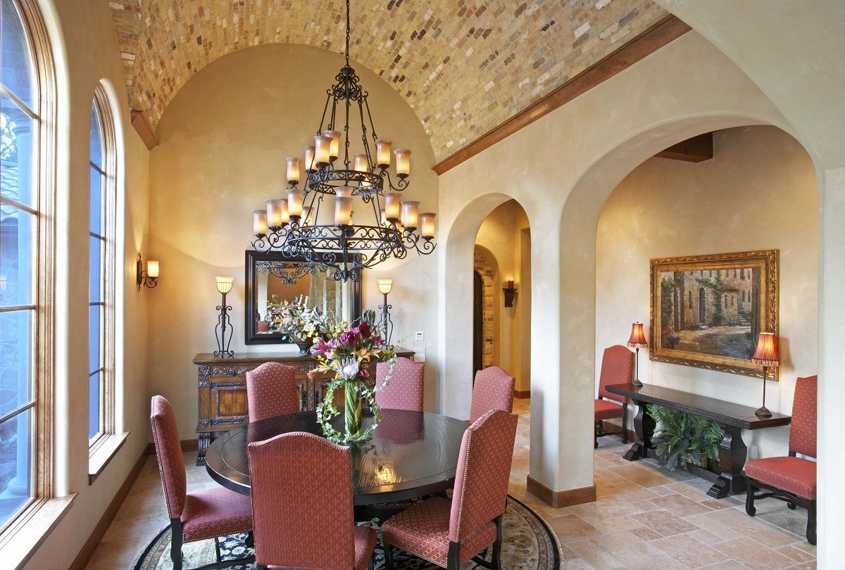 Elegant dining room with round table, ornate chandelier, arched doorways, and art.
