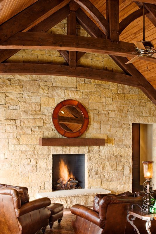 Stone fireplace with fire, brown leather chairs, arched ceiling with wood beams, and a round mirror.