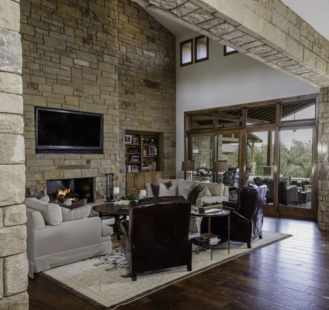 Living room with stone fireplace, TV, and view of outside through large windows.