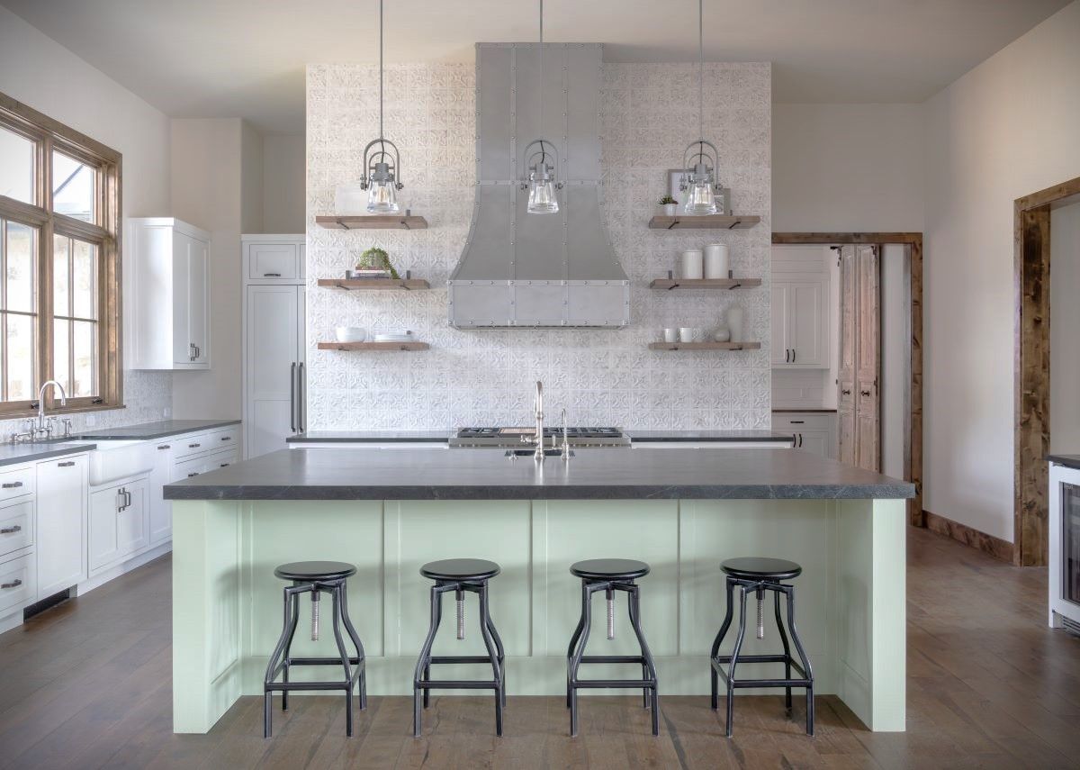 Kitchen with green island, black stools, white cabinets, and decorative shelves.