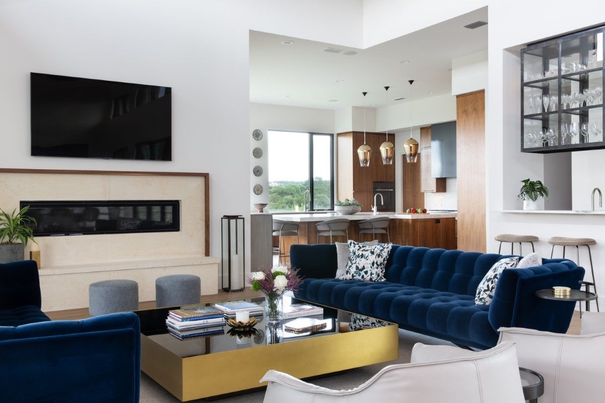 Luxurious living room with blue velvet sofa, fireplace, and open kitchen with gold accents.