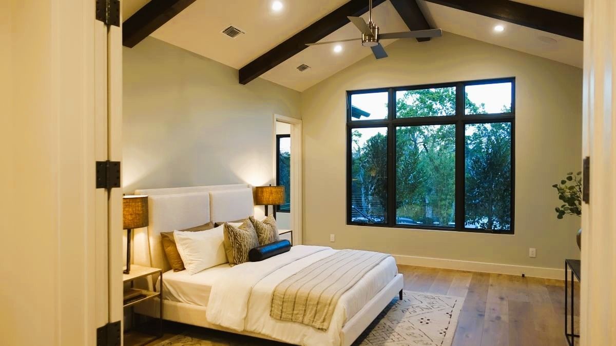 Bedroom with vaulted ceiling, large window, bed with pillows, and wood accents.