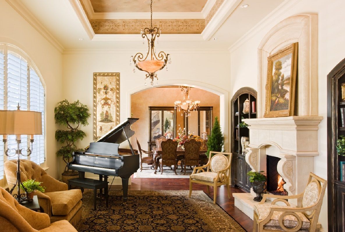 Elegant living room with grand piano, fireplace, chandelier, and archways.