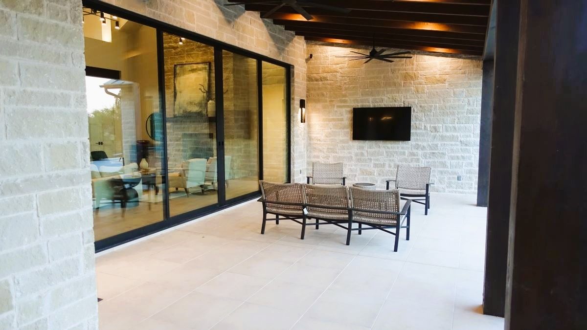 Patio with stone walls, glass sliding doors to a living space, seating, and a mounted TV.